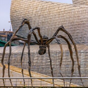 A large bronze spider sculpture stands outside a modern, metallic building in Bilbao, making it a must-see for any travel guide.
