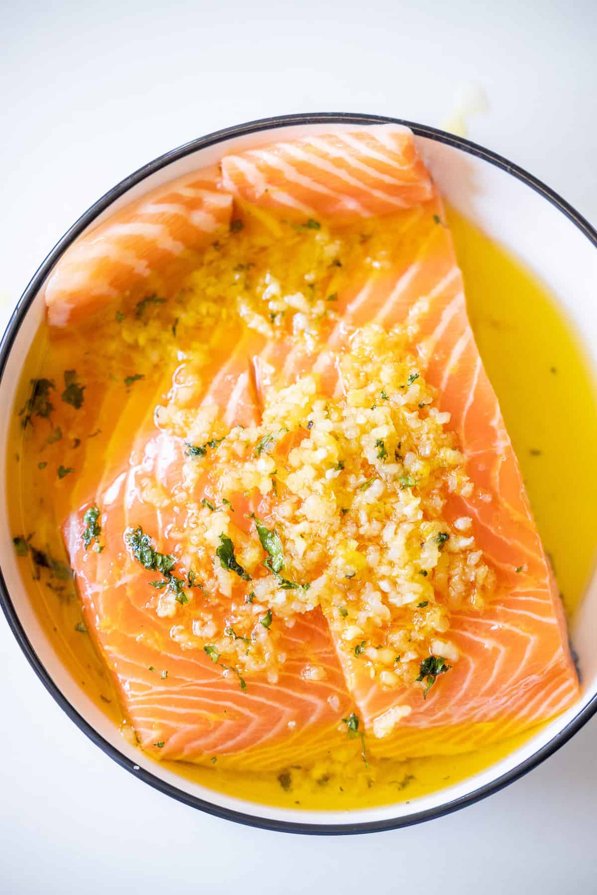 Raw salmon fillets marinating in a bowl with olive oil, minced garlic, herbs, and spices—perfect for an Easy Air Fryer Lemon Garlic Salmon Recipe.