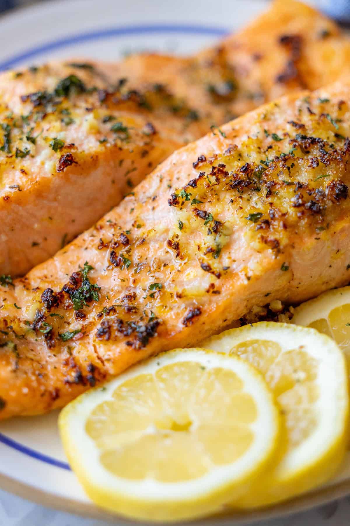 Two golden-brown, seasoned salmon fillets beautifully arranged on a white plate, accompanied by three glistening slices of fresh lemon. This visual encapsulates the simplicity and deliciousness of the Easy Air Fryer Lemon Garlic Salmon Recipe, ready to be served.