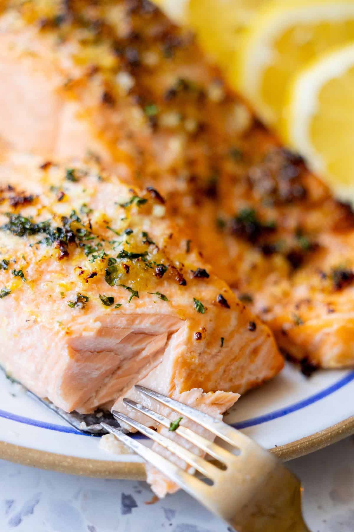 A fork flaking a piece of perfectly cooked air fryer salmon topped with fresh herbs, with vibrant lemon slices in the background. This image highlights the tender texture and aromatic flavors of an Easy Air Fryer Lemon Garlic Salmon Recipe, perfect for quick, healthy meals.