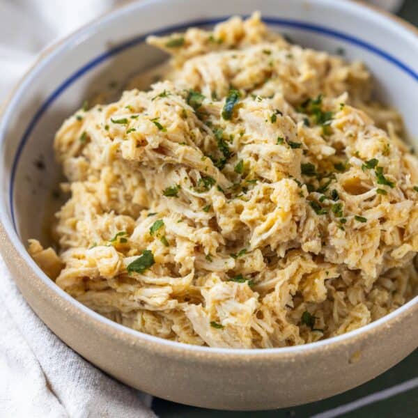 A bowl filled with shredded chicken—perfect for a Keto Shredded Chicken Recipe—topped with chopped herbs, placed on a light-colored surface next to a cloth napkin.