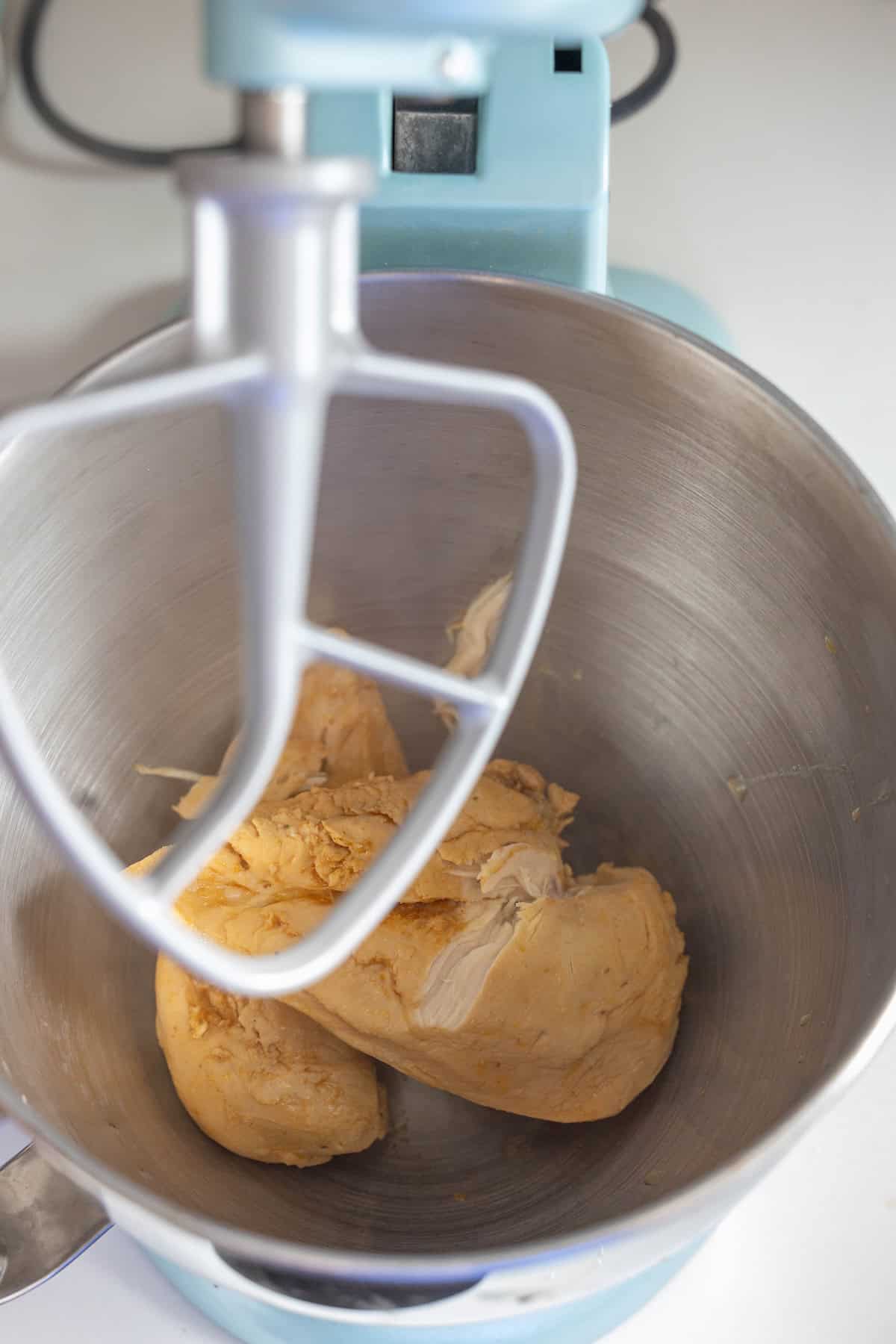 A ball of dough in the bowl of a stand mixer with a paddle attachment, perfect for whipping up meals like a Meal Prep boiled chicken recipe or a delicious Shredded Chicken Recipe.