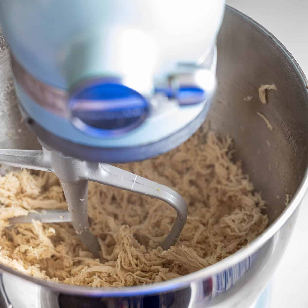 A stand mixer with a paddle attachment is shredding cooked chicken in a stainless steel mixing bowl—perfect for your Easy Boiled Chicken Recipe and effortless meal prep.