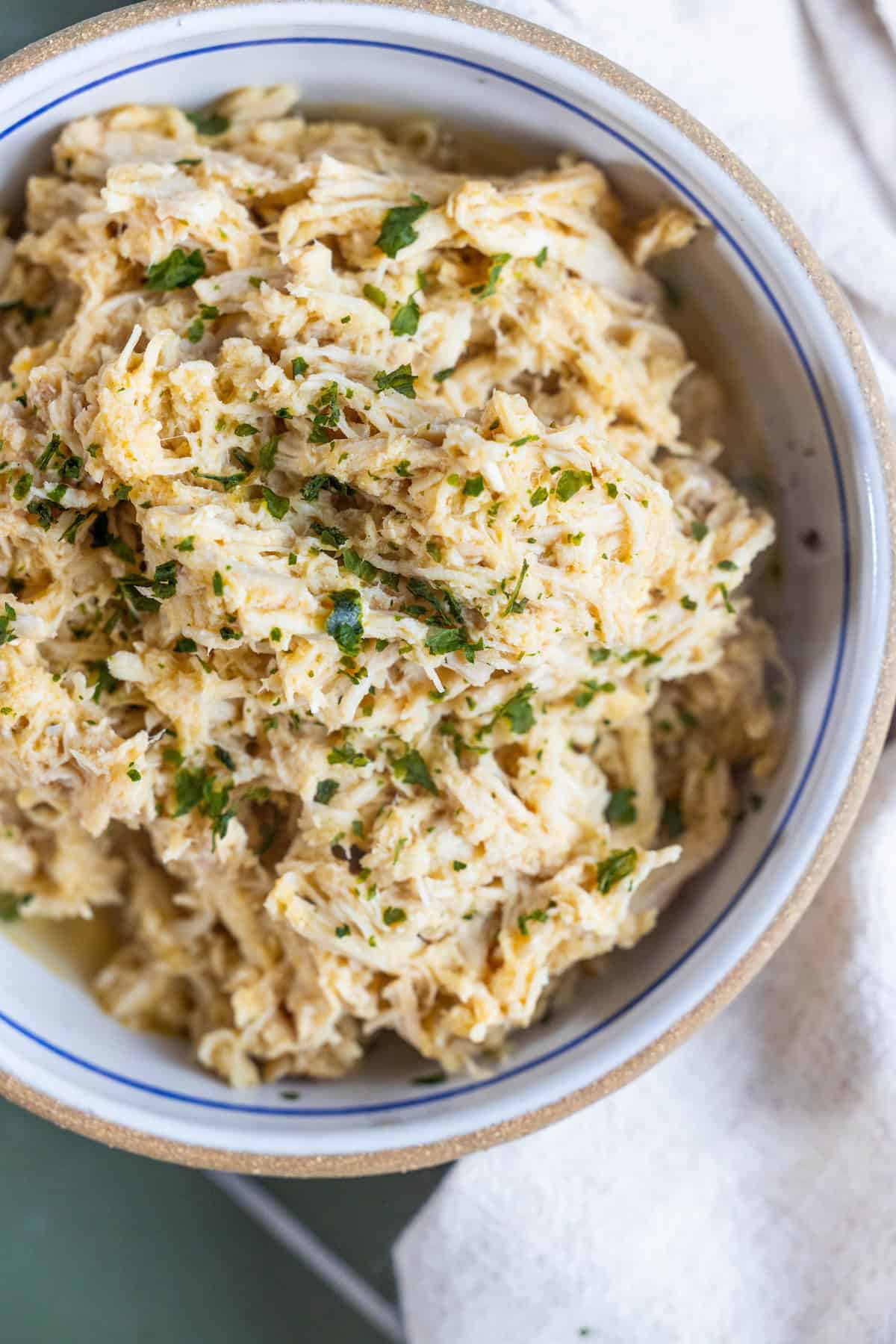 A bowl of shredded chicken topped with chopped herbs, served in a white dish with a beige rim—perfect for any meal prep boiled chicken recipe.
