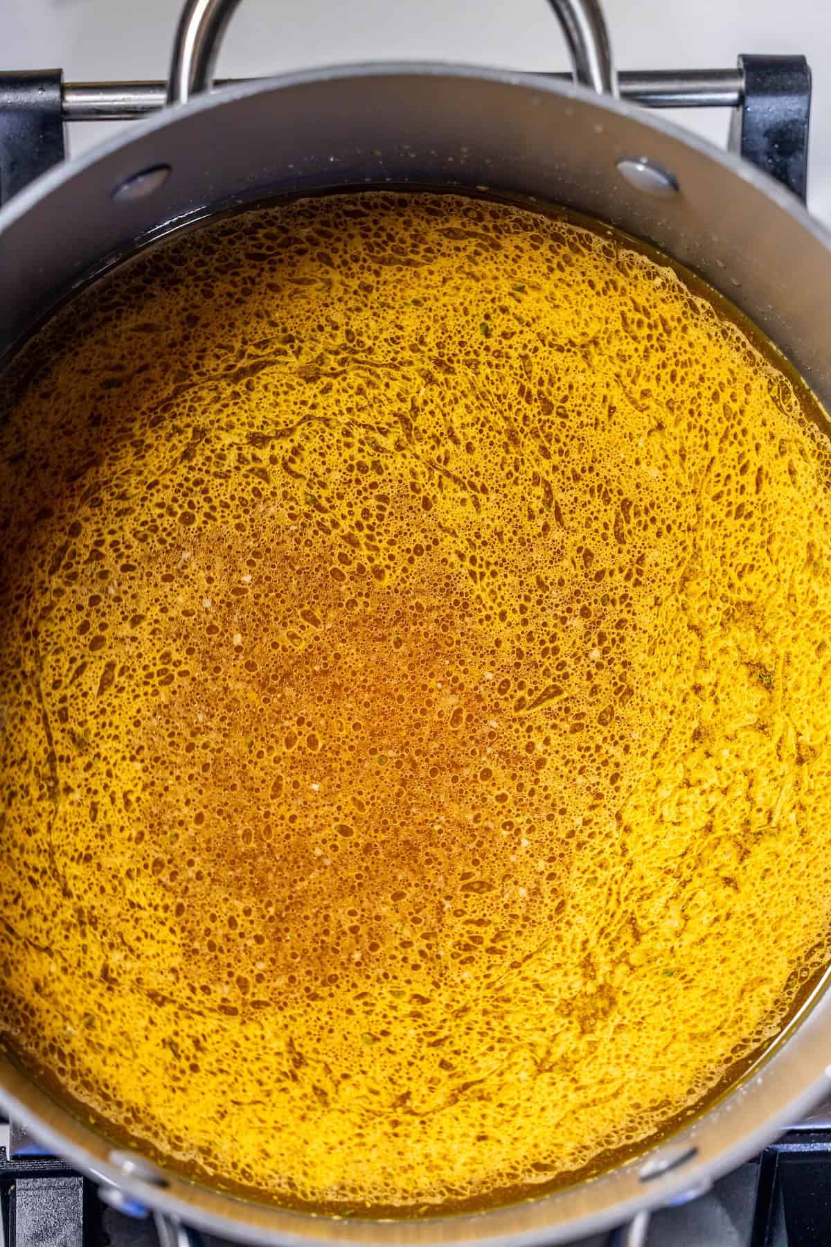 A large pot filled with golden brown broth simmers on the stove, with small bubbles and foam rising—a perfect scene for the Best Boiled Chicken or your favorite meal prep boiled chicken recipe.