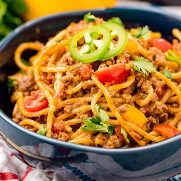 A bowl filled with one pot taco spaghetti cooked with minced meat, sliced cherry tomatoes, chopped bell peppers, and garnished with jalapeño slices and cilantro.