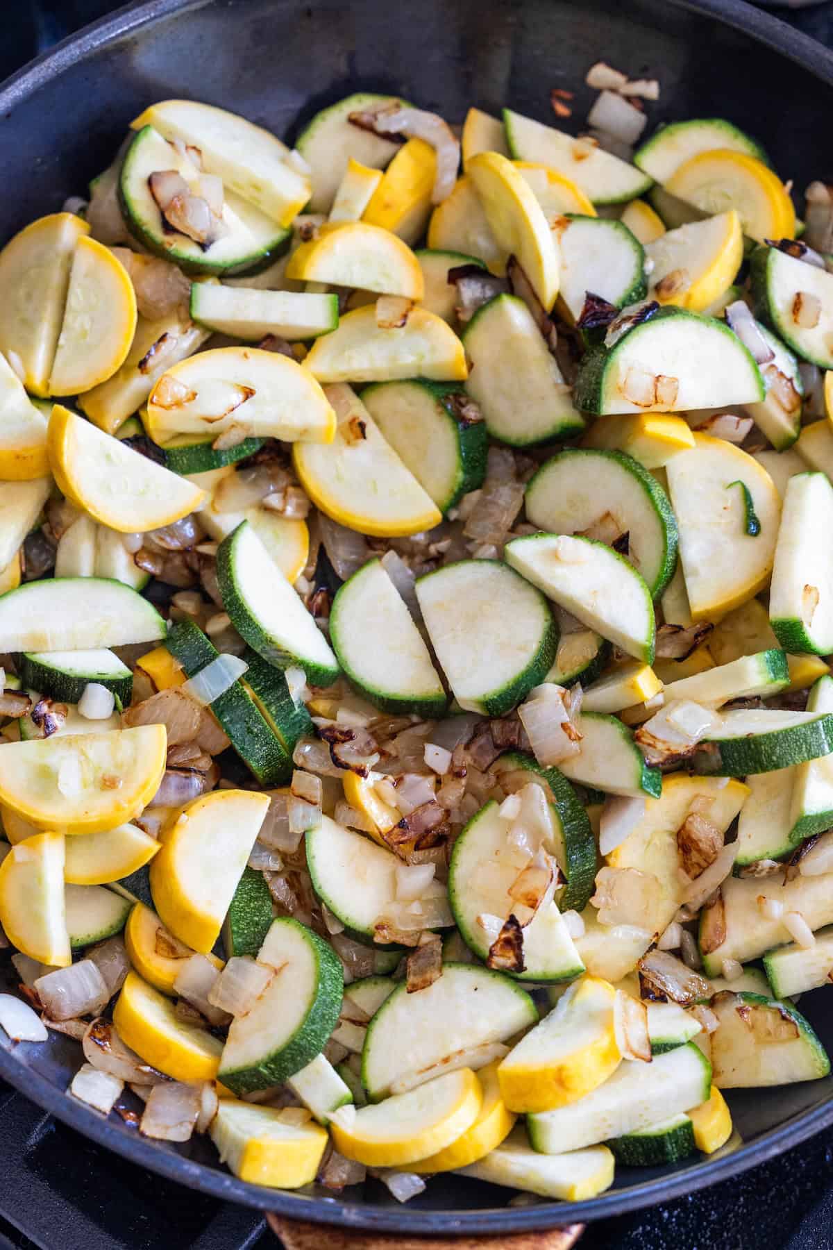 Sliced zucchini and yellow squash with chopped onions sautee in a black skillet for a tasty zucchini and squash side dish.