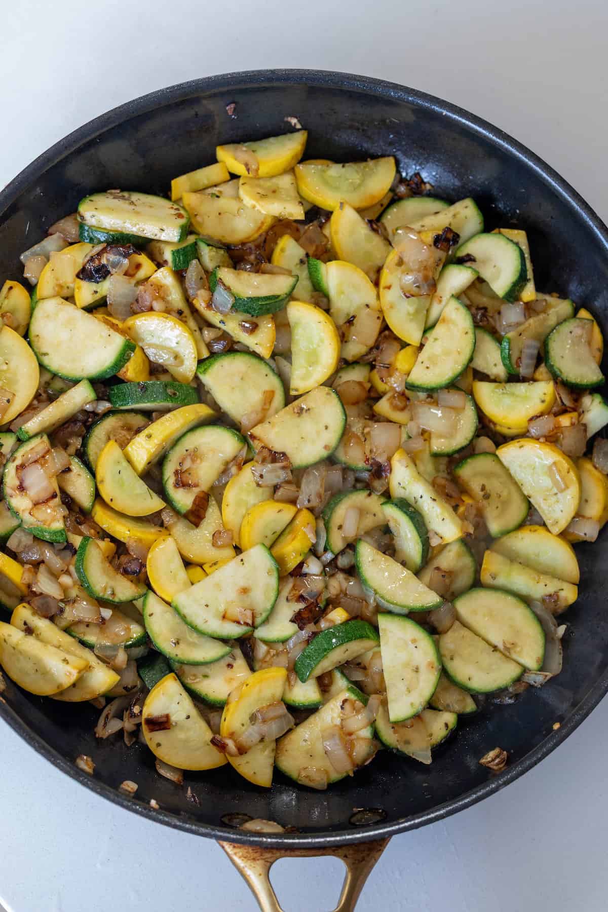 Sautéed sliced yellow squash, zucchini, and diced onions in a black skillet for a flavorful zucchini and squash side dish.
