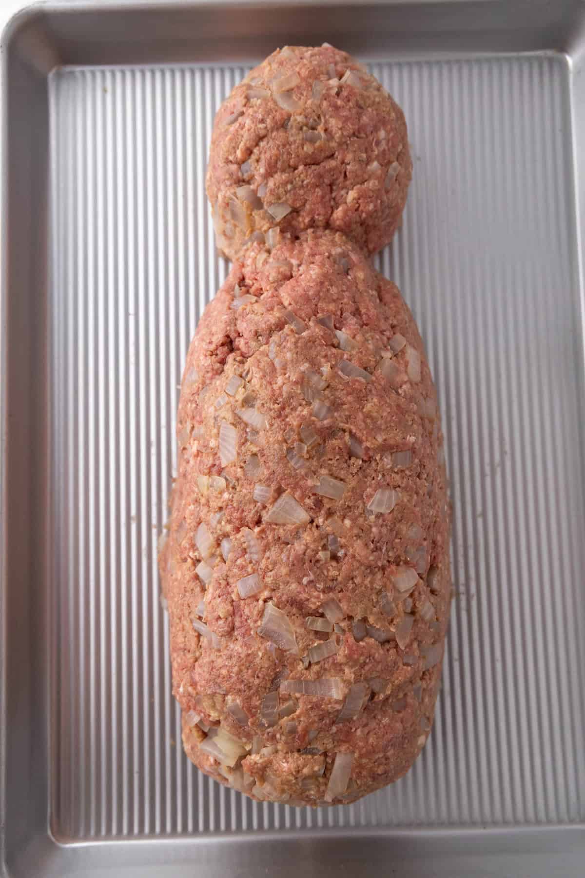 Ground meat mixed with diced onions, shaped into a rough figure resembling a mummy, placed on a metal baking tray.