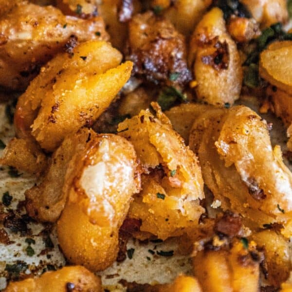 Close-up of crispy, pan-fried gnocchi with a golden-brown exterior, lightly seasoned with herbs and spices, accompanied by chili white beans.