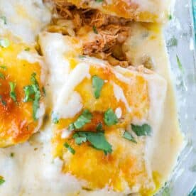 A close-up shot of cheesy chicken enchiladas topped with melted cheese and garnished with chopped cilantro in a glass baking dish.