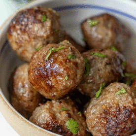 A bowl filled with several browned air fryer meatballs, garnished with small pieces of chopped fresh herbs.