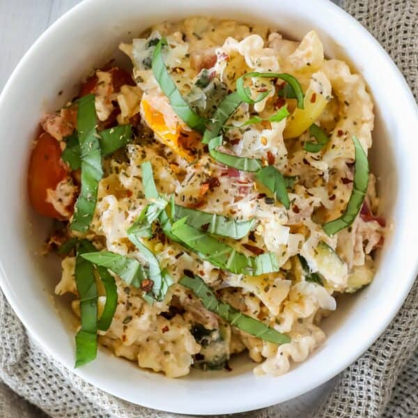 A bowl of pasta salad with mixed vegetables, topped with chopped basil and seasoning.