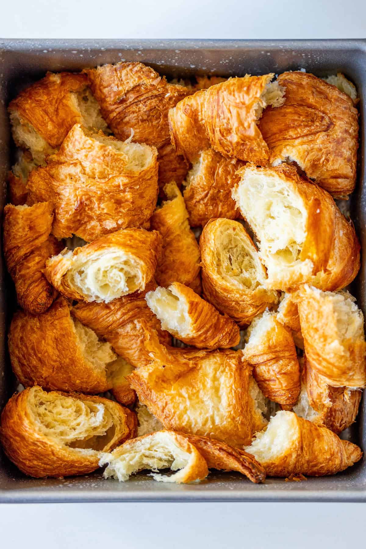 A tray filled with crispy, broken Ham and Cheese Croissant Strata pieces.