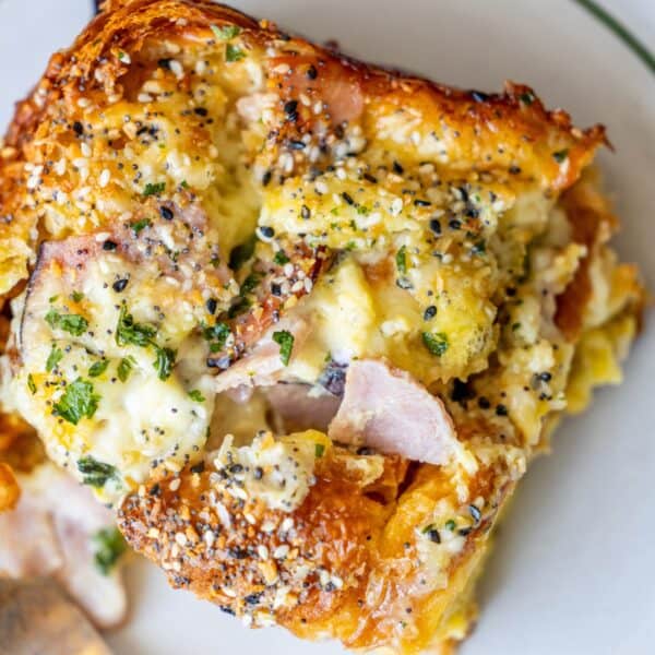 Close-up of a savory dish featuring ham, melted cheese, and an Everything Bagel seasoning blend on a croissant strata.