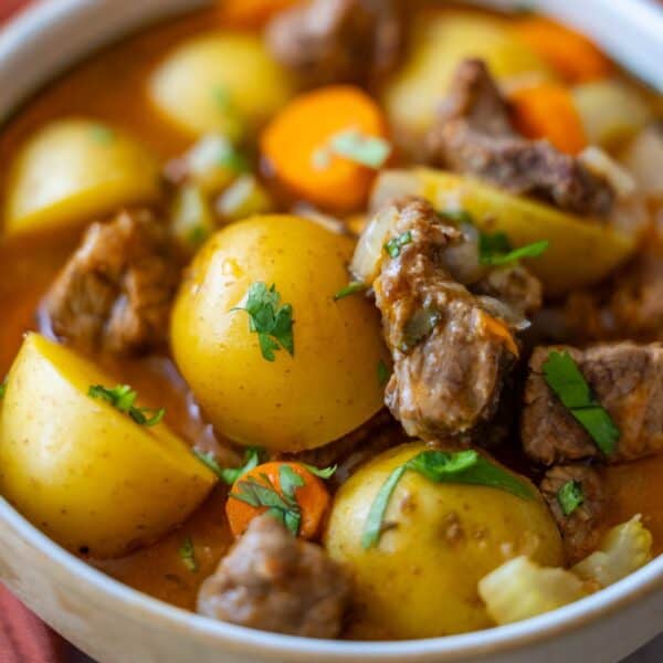 Close-up of a bowl filled with a hearty Classic Beef Stew consisting of chunks of beef, potatoes, and carrots, garnished with fresh parsley. The broth appears thick and seasoned.