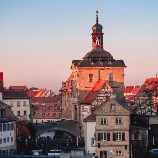 Historic building with timber-framed architecture in Bamberg, Germany, under a clear sky at sunset, surrounded by European-style rooftops. During the Christmas market season, the glowing lights add a magical touch to this picturesque scene.