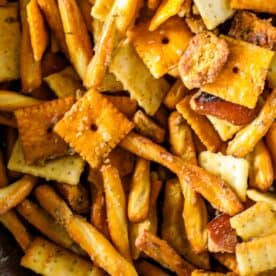 A close-up of a smoked trail mix featuring pretzel sticks, square cheese crackers, and seasoned bread pieces.