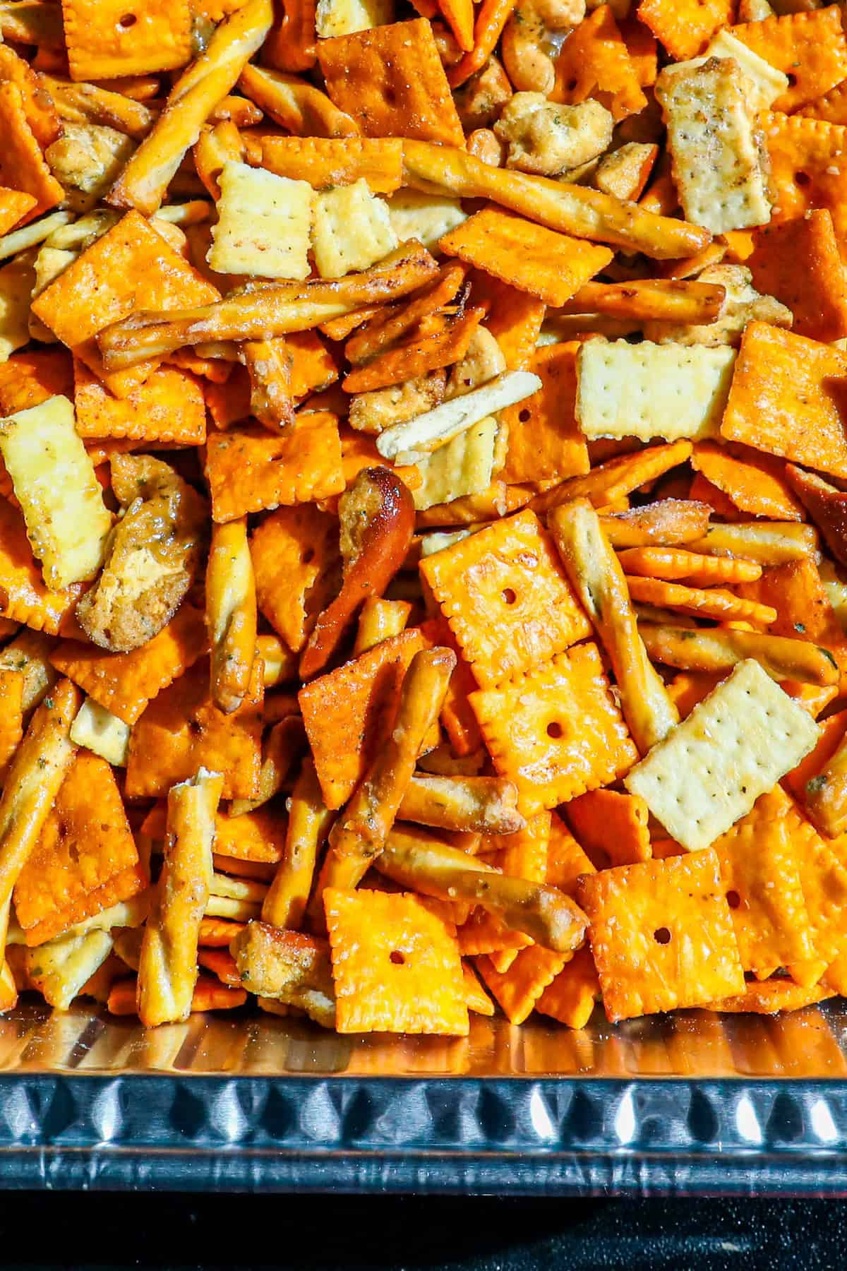 A close-up of smoked trail mix on a tray, featuring orange cheese crackers, white square crackers, small pretzel sticks, and pretzel twists.