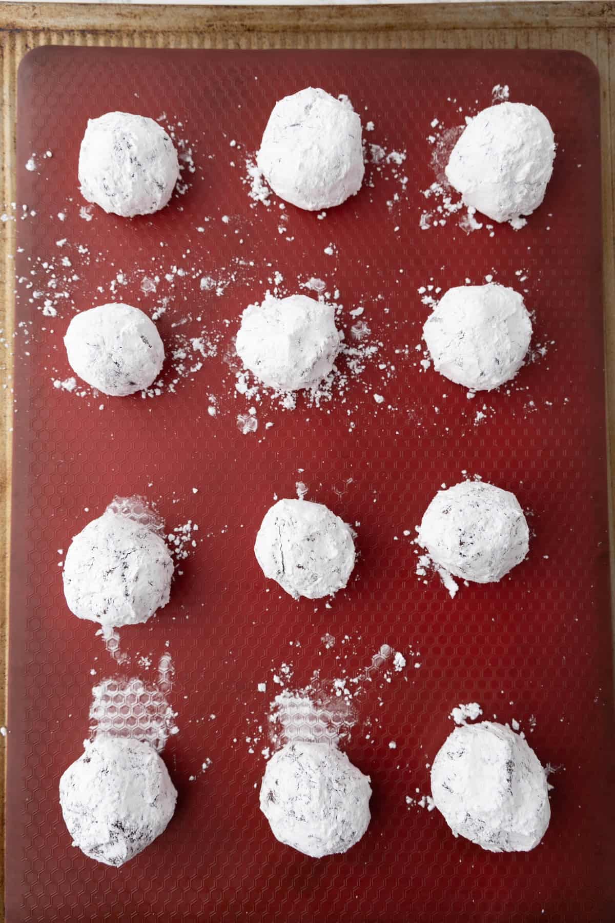 Twelve chocolate crinkle cookies, dusted with powdered sugar, are arranged on a red baking sheet.