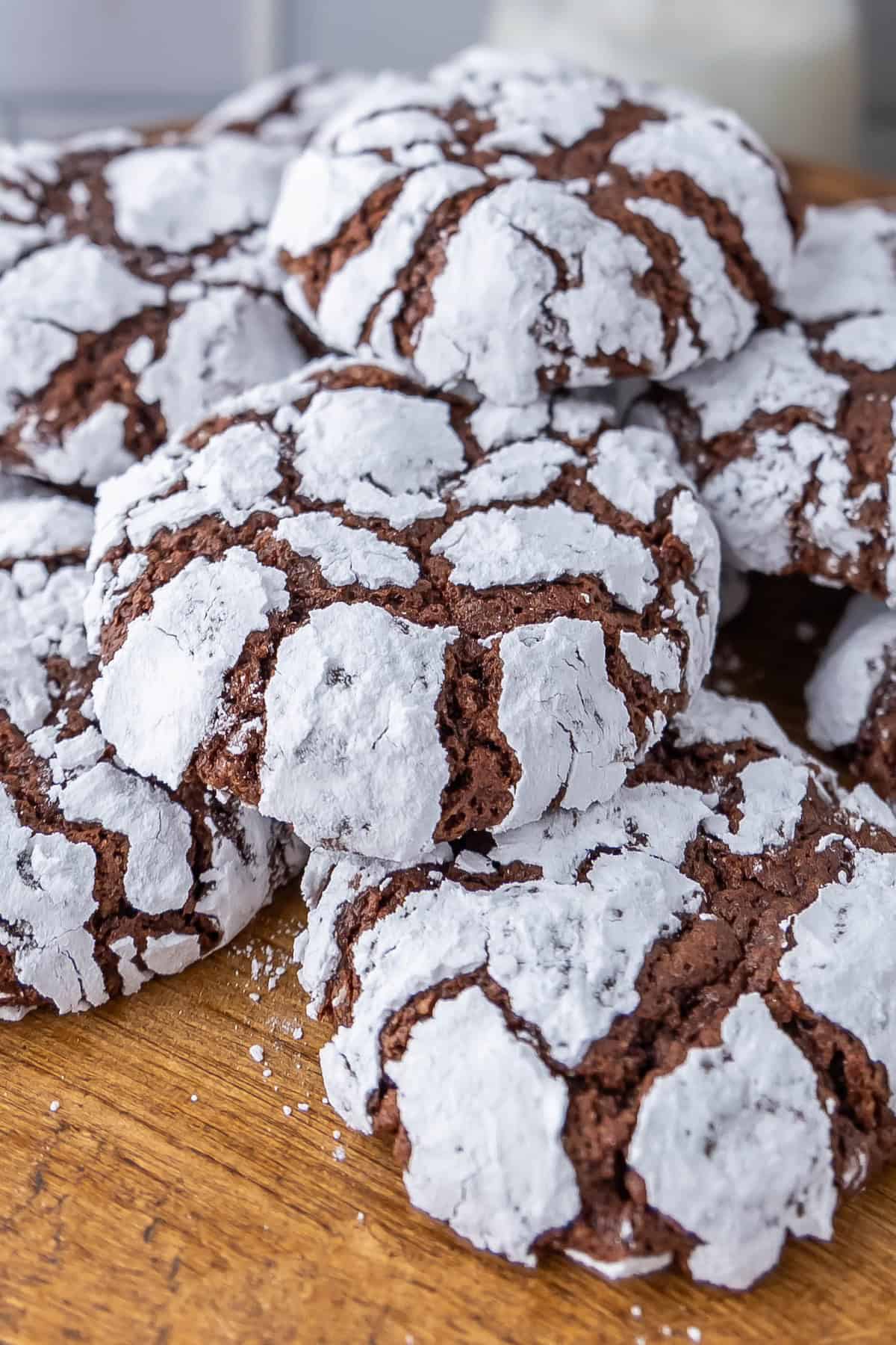 A delightful pile of chocolate crinkle cookies, dusted with powdered sugar, rests invitingly on a rustic wooden surface.