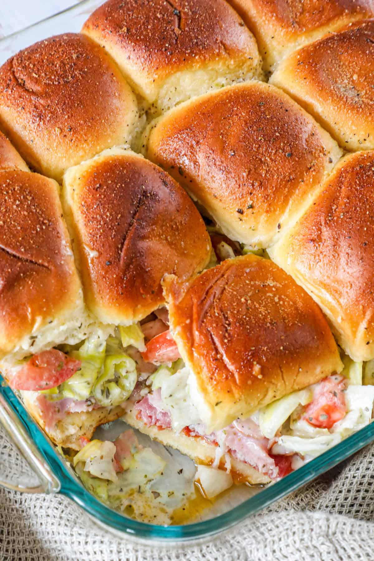 A glass baking dish with a batch of baked sliders filled with lettuce, tomato, and bacon.