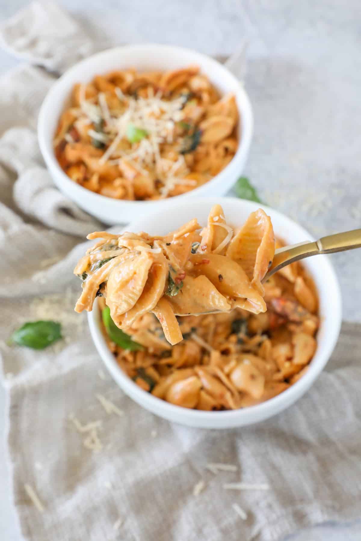 Two bowls of creamy pasta shells with herbs and cheese on top. A fork holds a portion above one bowl.