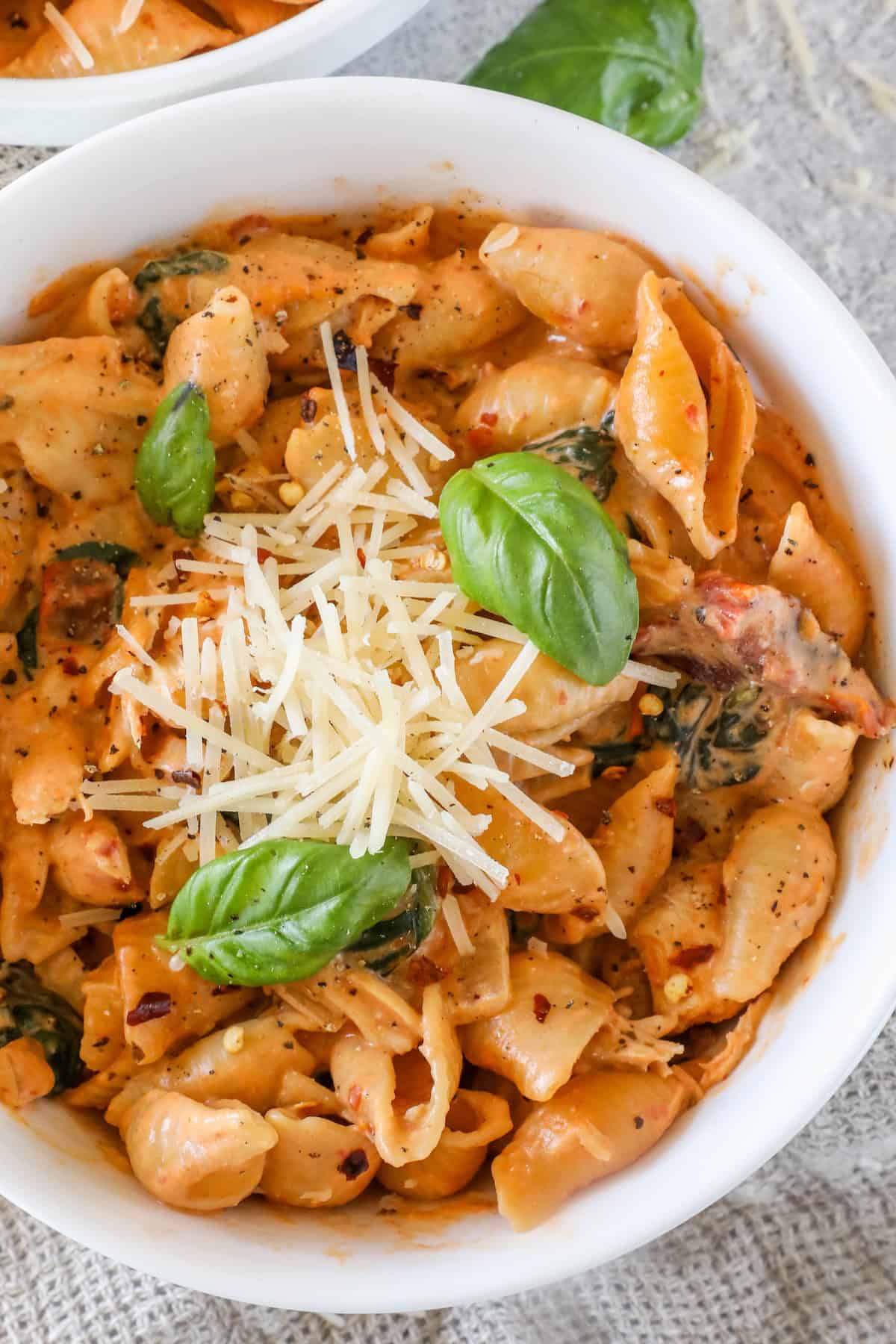 A bowl of creamy pasta with tomato sauce, topped with shredded cheese and fresh basil leaves.