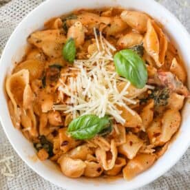 A bowl of creamy pasta with shell noodles, topped with grated cheese and basil leaves.