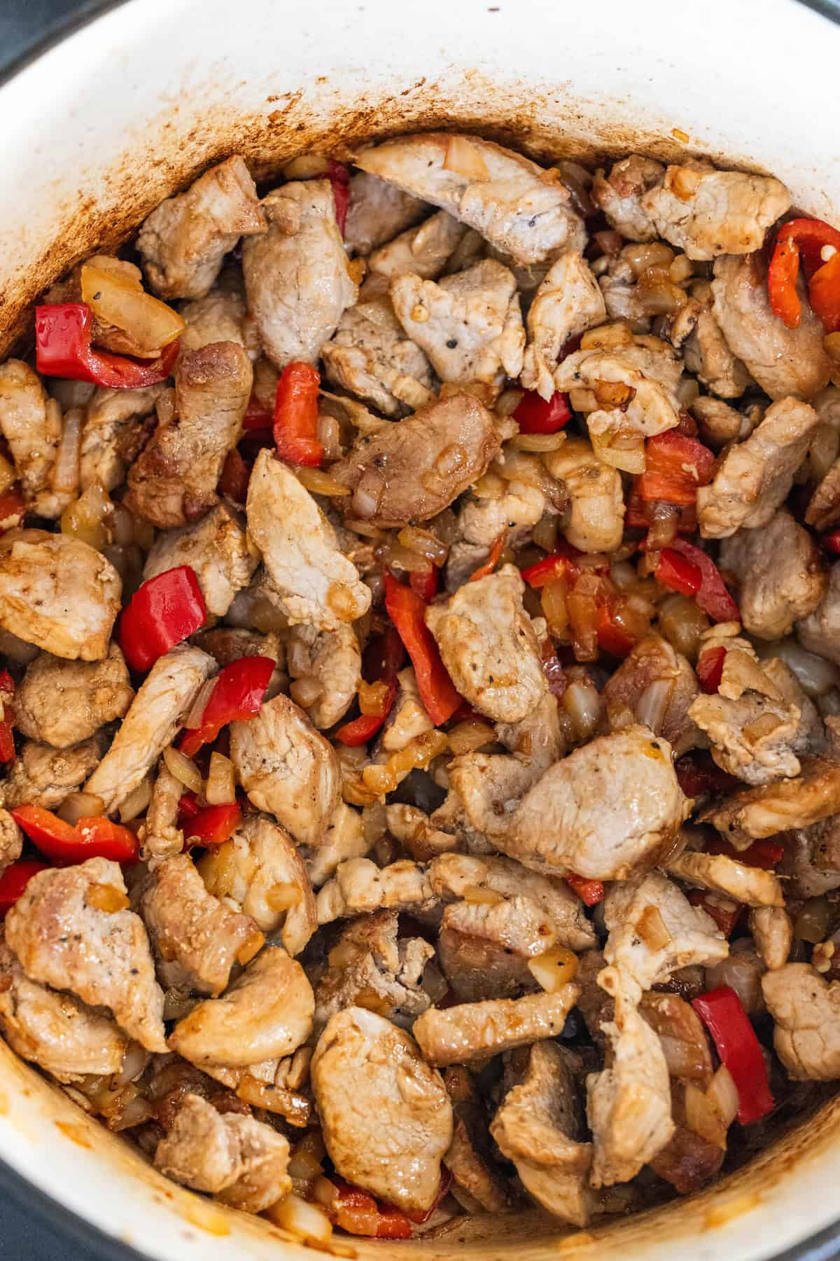 A pot filled with succulent Pork Paprikash, featuring tender pork pieces, vibrant red bell peppers, and onions.
