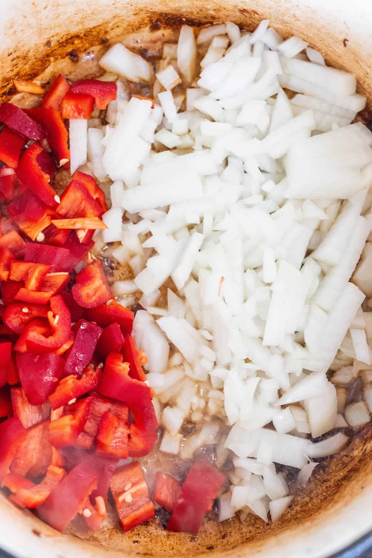 Chopped red bell peppers and onions are sautéing in a pan, creating a colorful mixture on a seasoned surface, forming the perfect base for a flavorful Pork Paprikash.