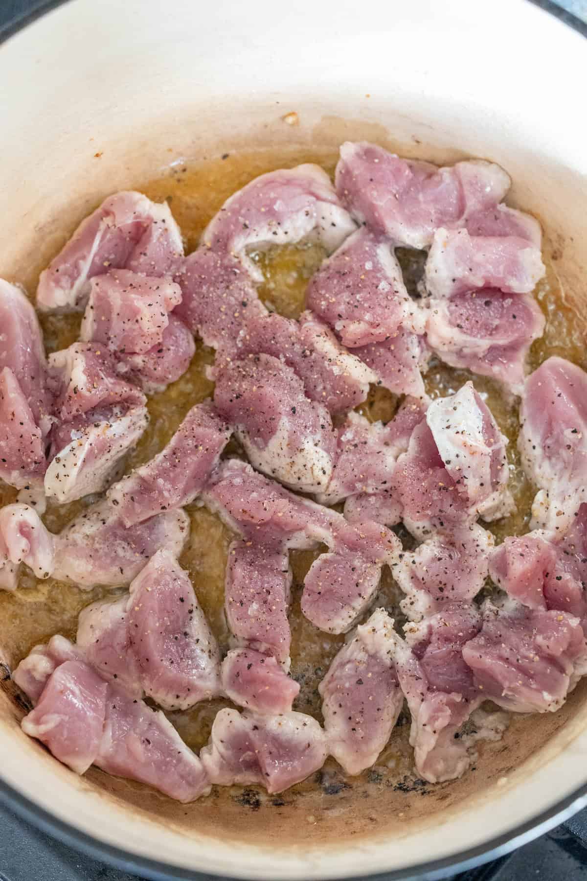 Savory Pork Paprikash, featuring raw pieces of seasoned pork, simmers gently in a pot.
