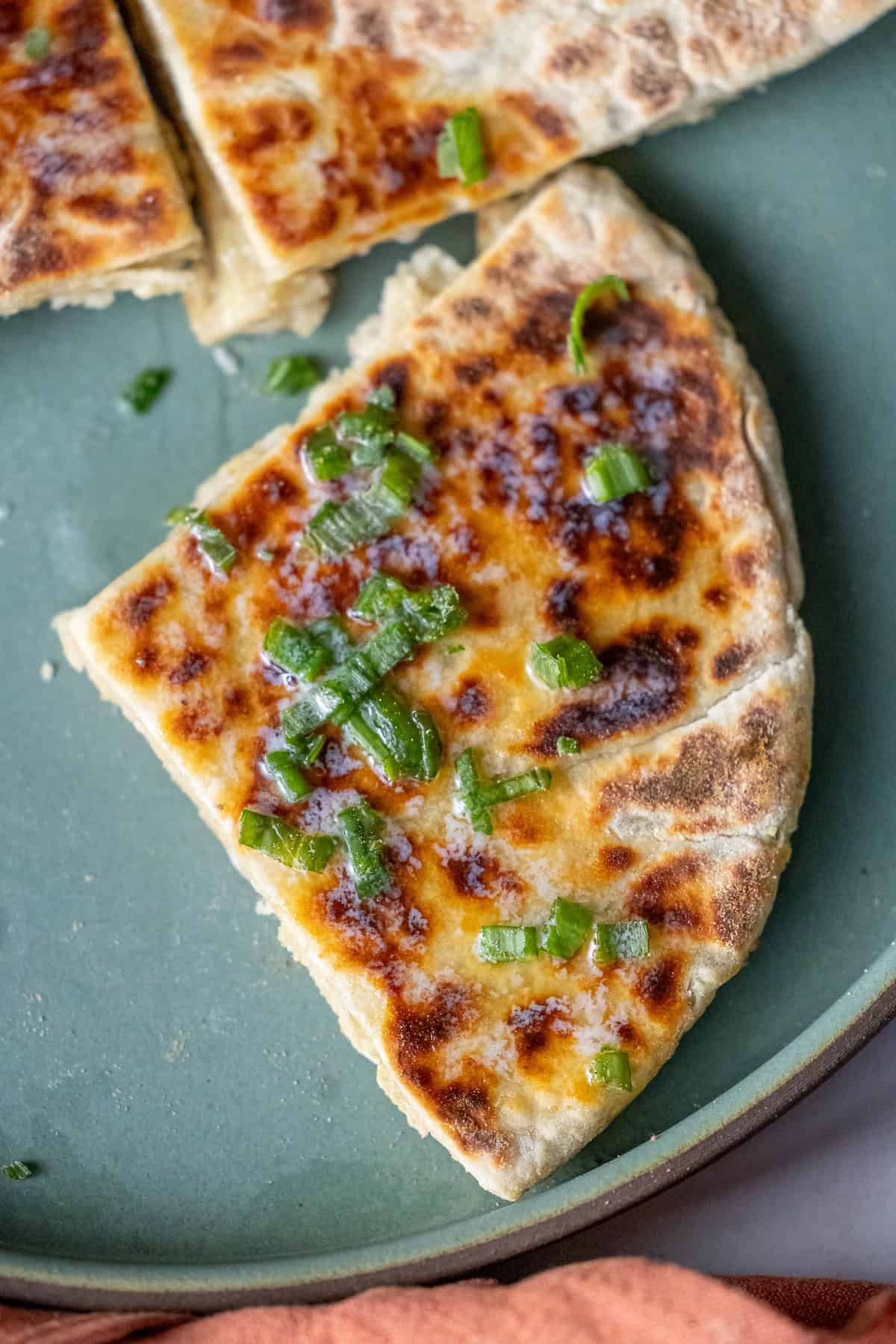 A slice of stuffed flatbread, reminiscent of a Scottish tattie scone, is topped with chopped green onions and rests on a green plate.