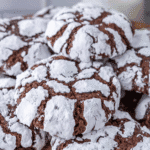 A close-up of several chocolate crinkle cookies coated in powdered sugar, highlighting the distinctive cracked surface pattern that makes chocolate crinkle cookies a favorite treat.