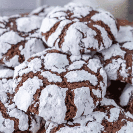 A close-up of several chocolate crinkle cookies coated in powdered sugar, highlighting the distinctive cracked surface pattern that makes chocolate crinkle cookies a favorite treat.