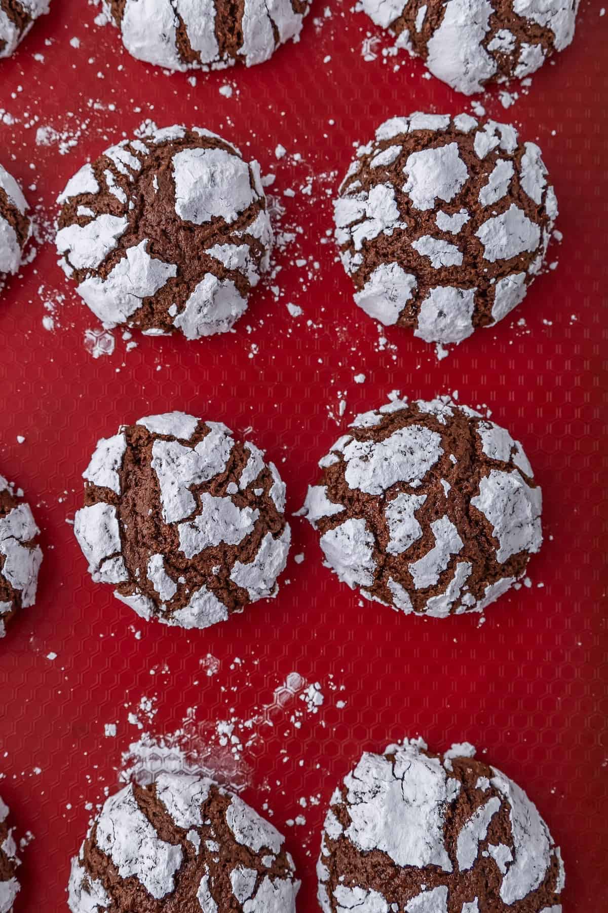 Chocolate crinkle cookies with powdered sugar on a red baking mat.
