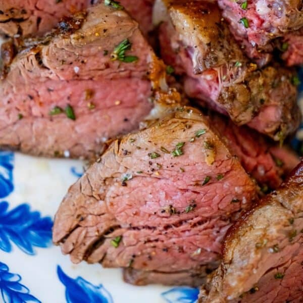 Close-up of medium-rare tenderloin steak slices on a white plate with blue floral patterns, garnished with herbs. The reverse sear method perfectly enhances the beef's flavor and juiciness.