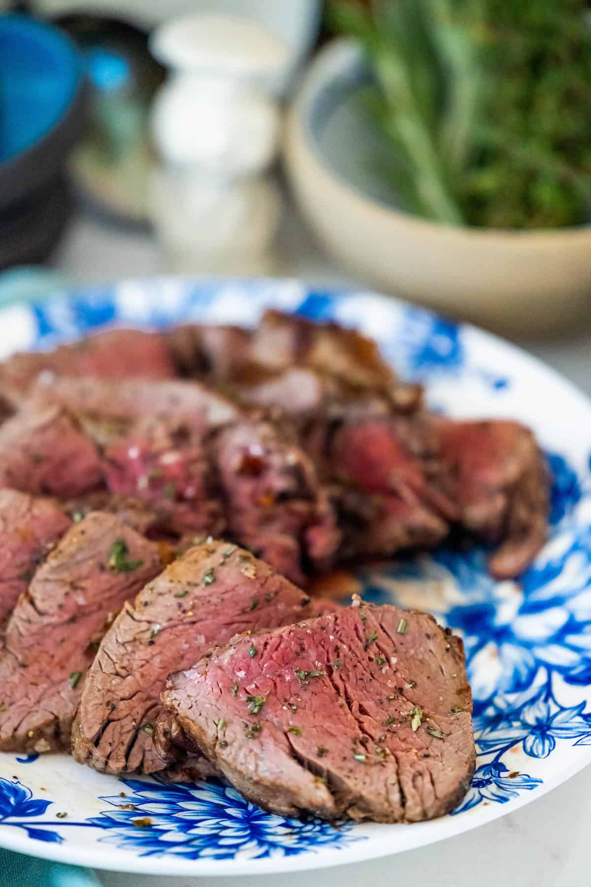 Sliced medium-rare beef tenderloin graces a blue and white plate, with herbs delicately sprinkled on top—a perfect reverse sear triumph.