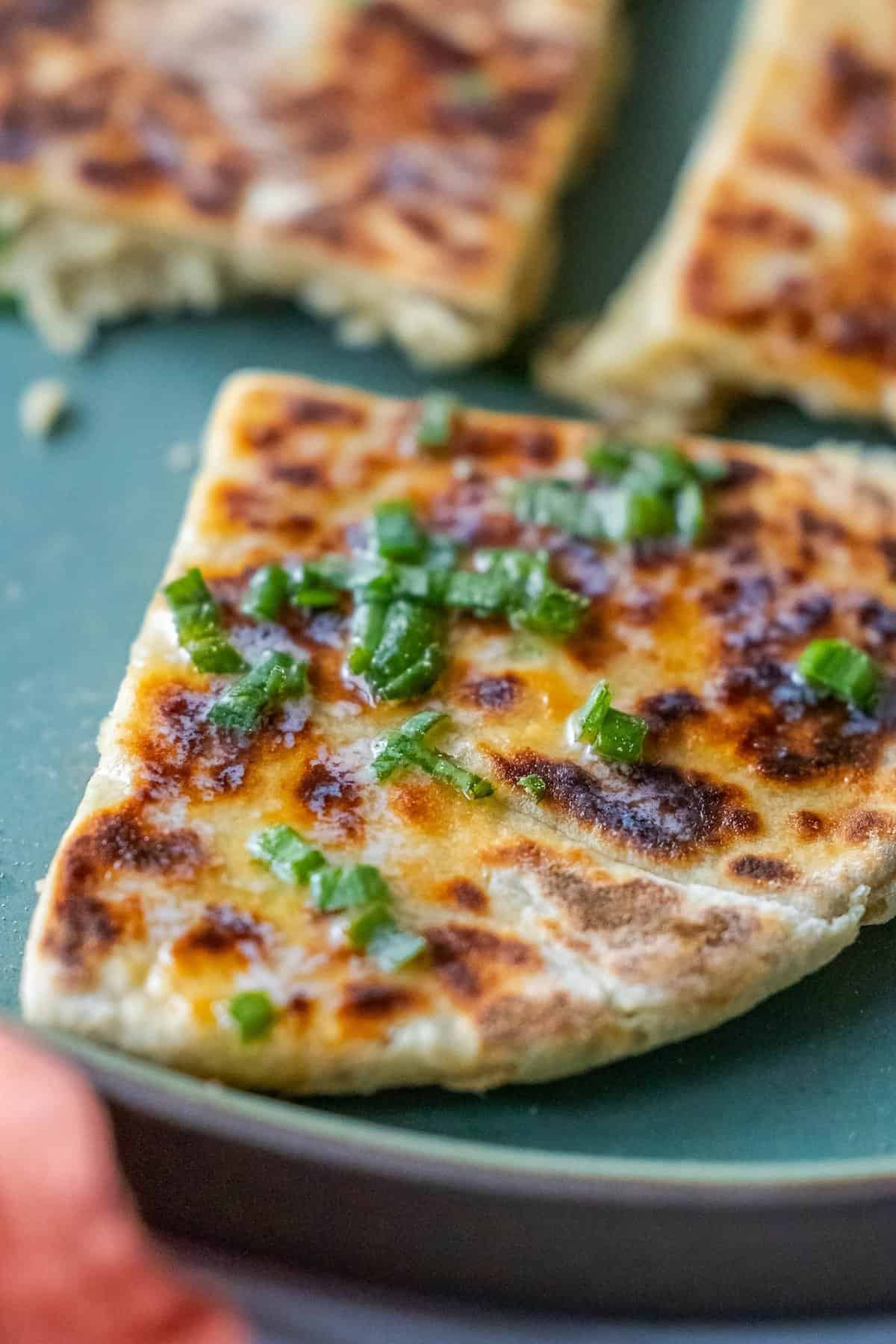 A triangular piece of pan-fried tattie scone garnished with chopped green onions rests enticingly on a green plate.