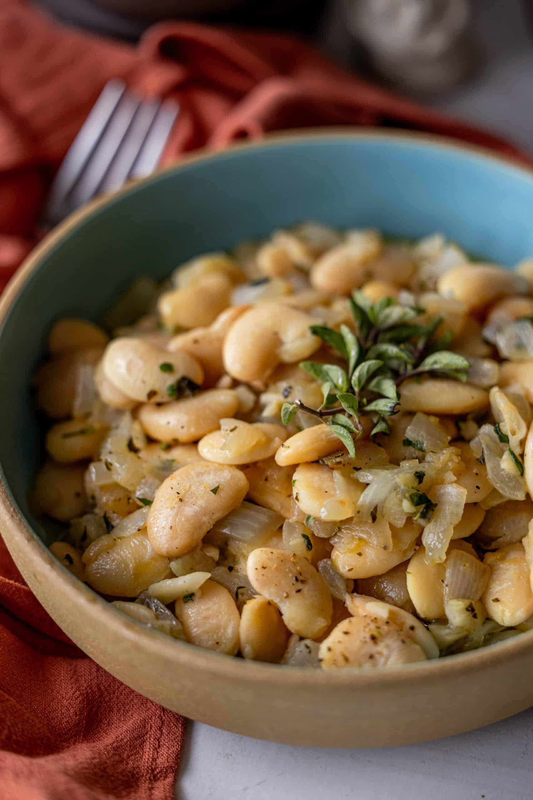 A bowl of cooked butter beans with onions and aromatic herbs, featuring a hint of garlic and garnished with fresh basil leaves.