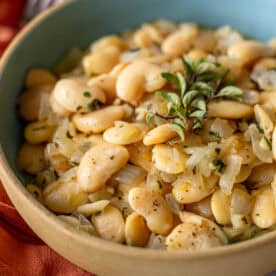 A bowl of cooked butter beans mixed with chopped onions, garlic, and garnished with fresh oregano.