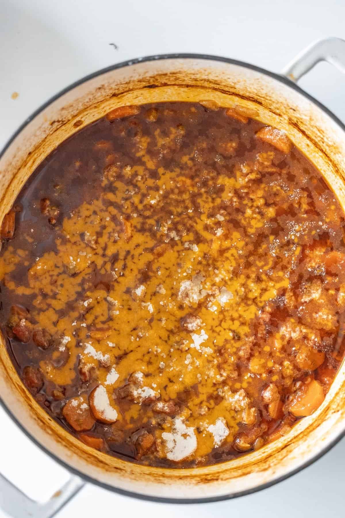 Top view of a large pot filled with a rich, brown stew featuring braised chunks of meat and vegetables, subtly seasoned with paprika.