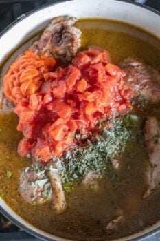 A pot with braised, seasoned meat, chopped tomatoes, paprika, and herbs gently simmering in a rich broth.