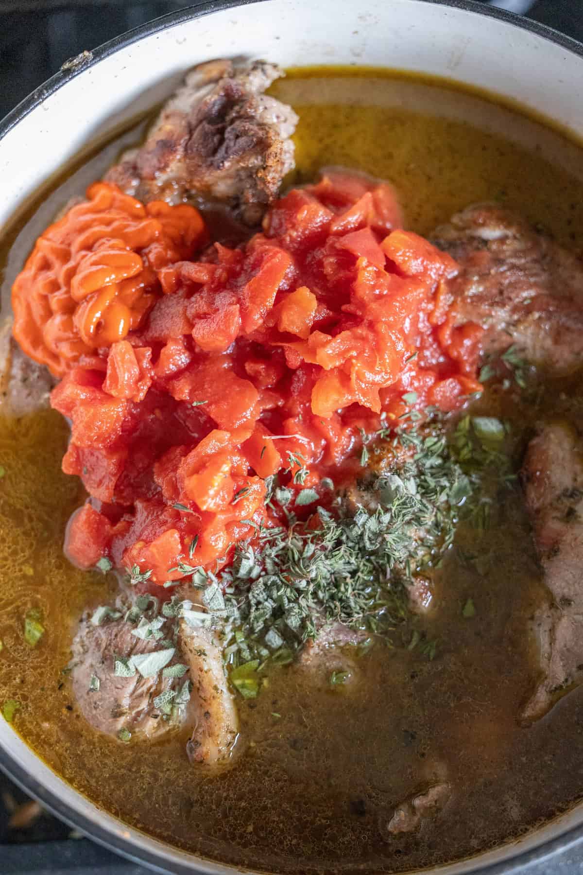 A pot with braised, seasoned meat, chopped tomatoes, paprika, and herbs gently simmering in a rich broth.