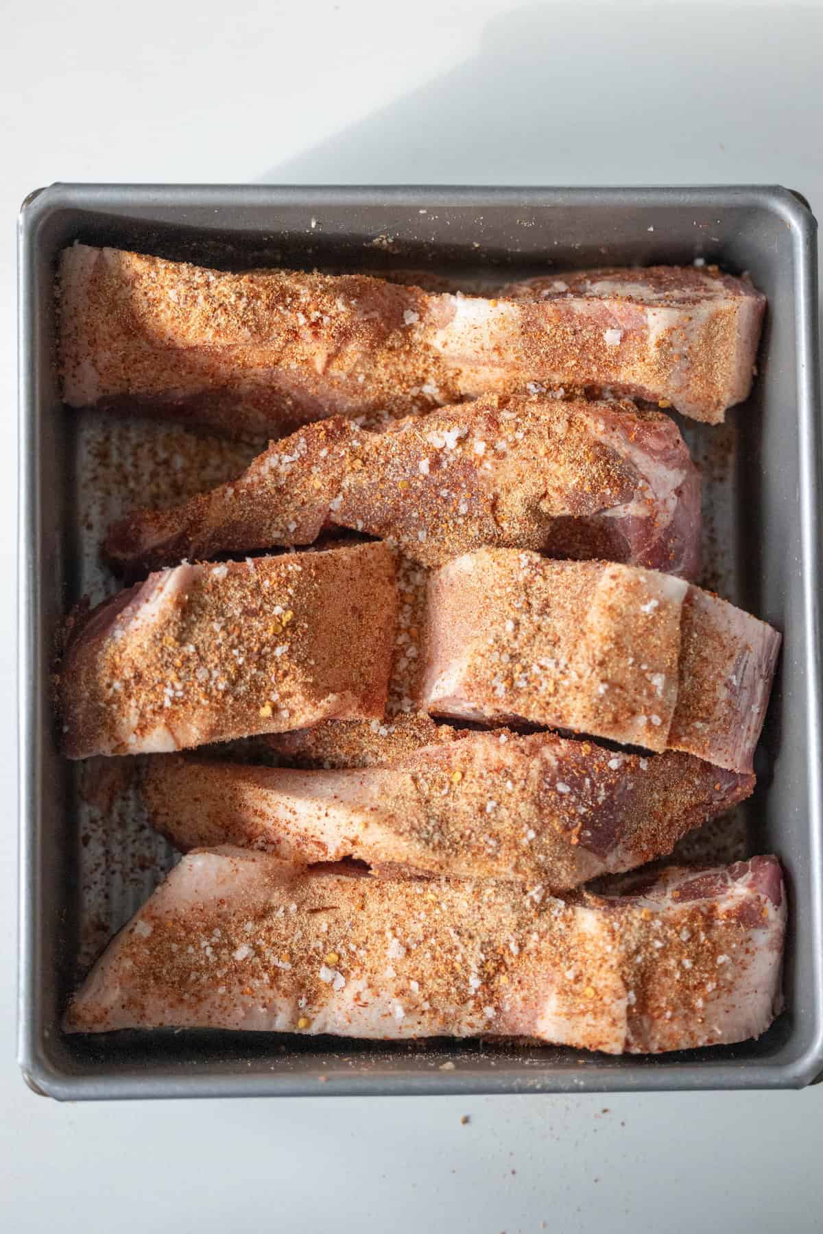 Country style ribs seasoned with dry spices rest in a metal pan, ready to be oven roasted to perfection.