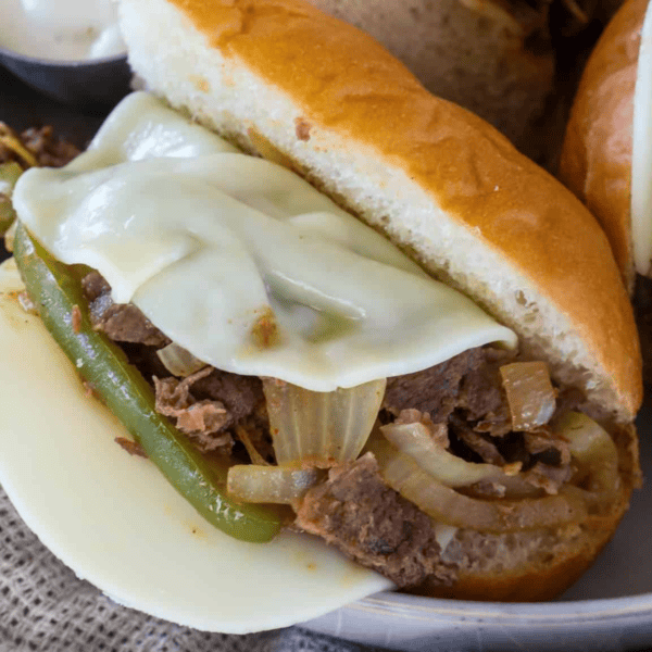 A close-up of a classic Philly Cheesesteaks sandwich featuring sliced beef, melted cheese, green peppers, and onions nestled in a hoagie roll.