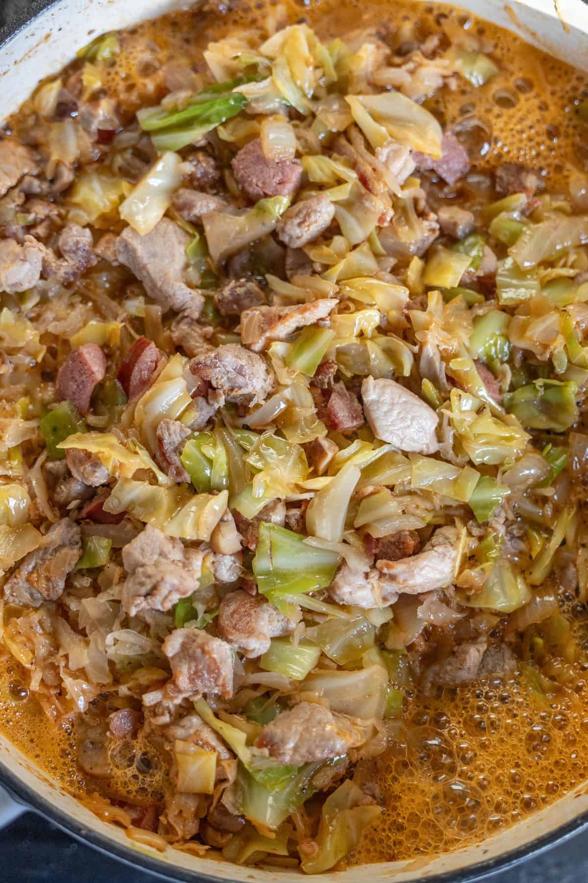 A close-up of a pot containing Bigos, the traditional Polish Hunter's Stew, made with cabbage, sliced meat, and sausages in a rich, simmering broth.