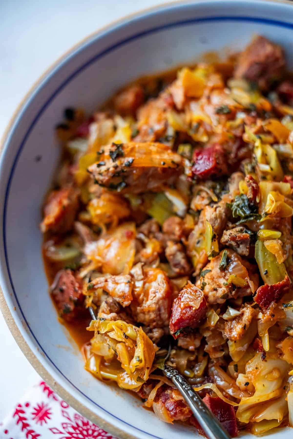 A bowl of hearty Polish Bigos, also known as Hunter's Stew, filled with sausage pieces, herbs, and diced vegetables, with a spoon ready to dive into the dish.
