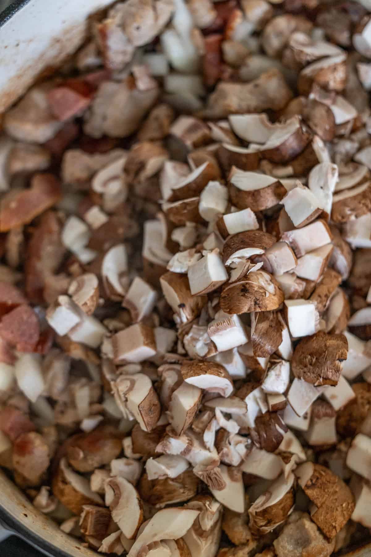 Chopped mushrooms and pieces of bacon sizzle in a pan, creating the savory base for a traditional hunters stew that delights with each bite.