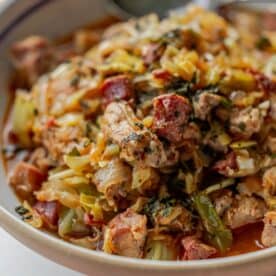 A close-up of a hearty Polish dish, Bigos, featuring chopped meat, cabbage, and vegetables in a bowl, garnished with fresh herbs.